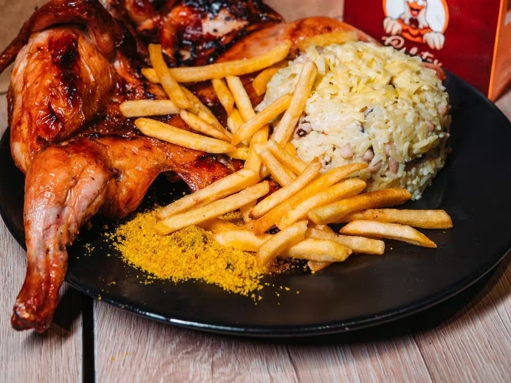 Prato cheio com galeto assado na brasa, batata frita, baião de dois e farofa